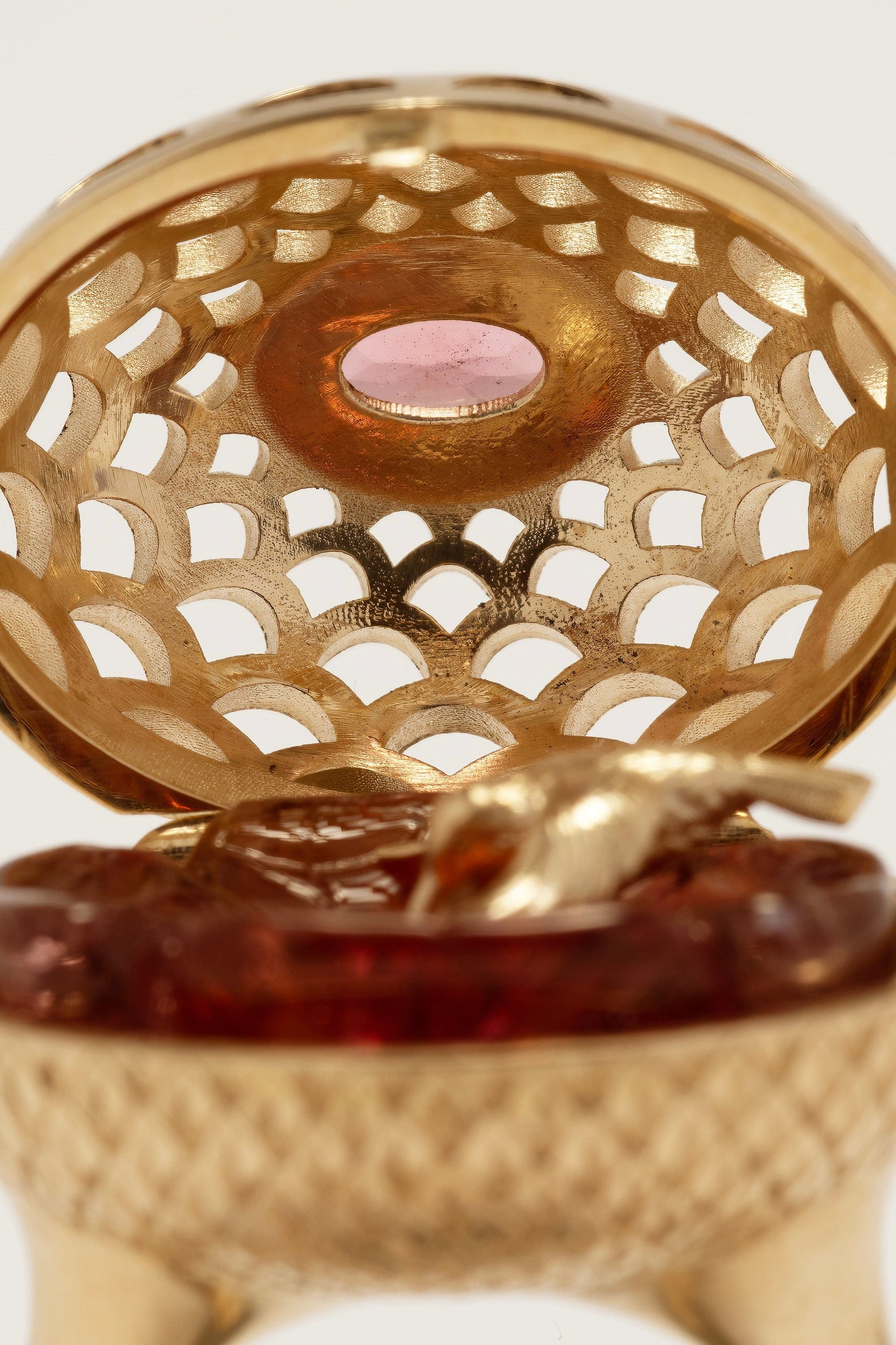 Close-up of a gold container with a pink stone and red substance inside.