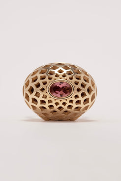 Gold decorative ball with a pink gemstone on a light gray background