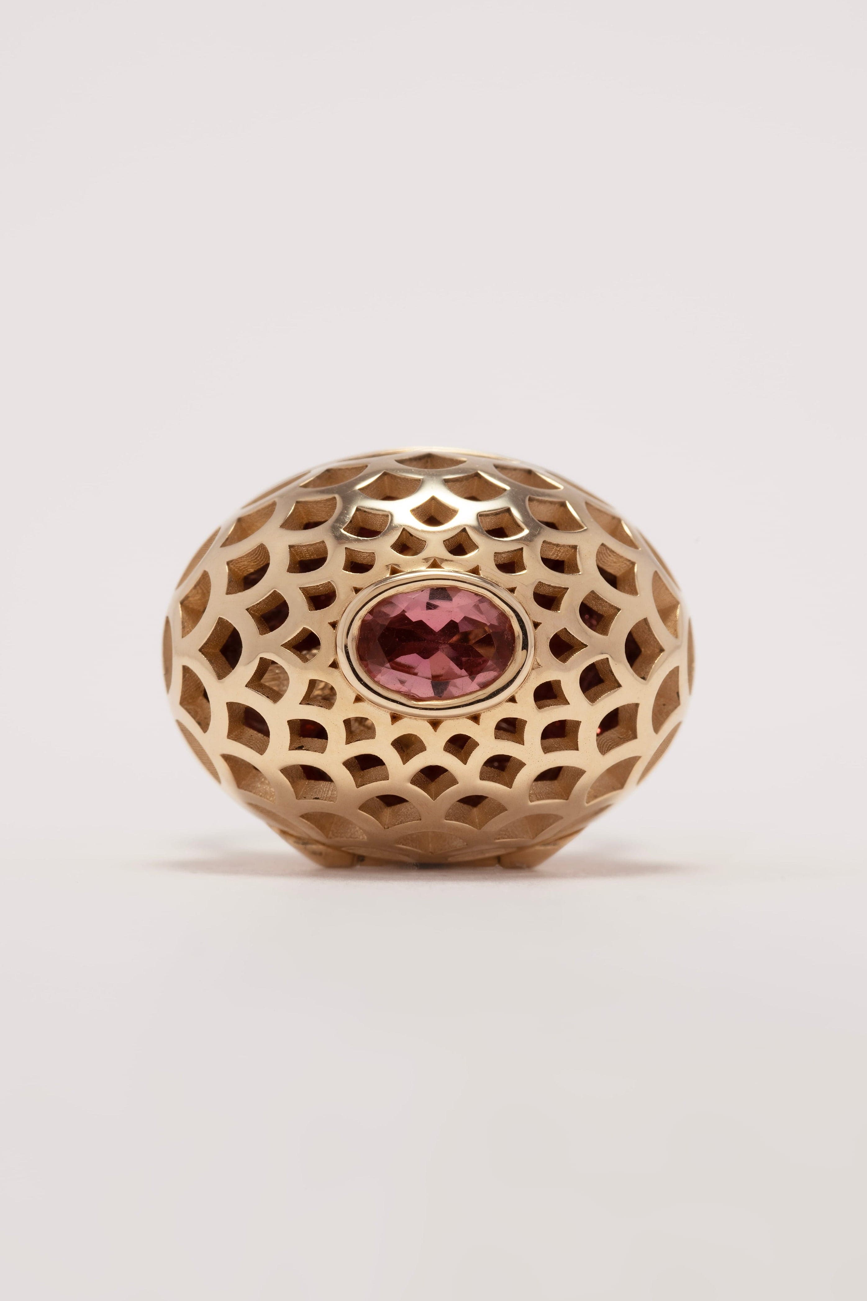 Gold decorative ball with a pink gemstone on a light gray background